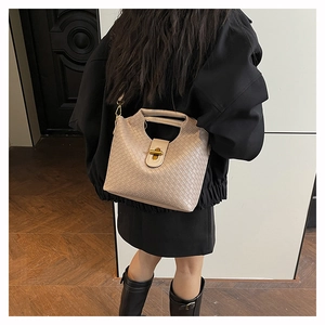 Detail of beige woven leather crossbody bag with metallic clasp worn by a model