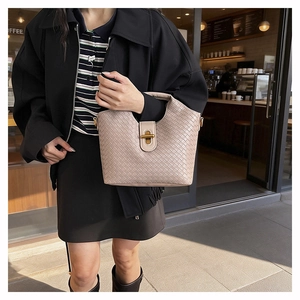 Detail of woven beige leather tote bag featuring a golden metal twist lock and handle