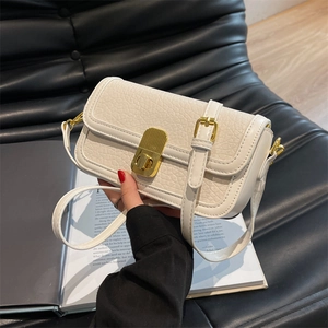 Detail of white lychee leather texture and gold hardware lock on crossbody bag