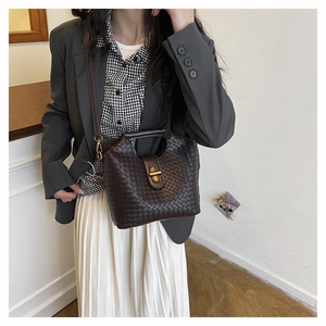 Close-up of brown woven shoulder bag with a gold metal twist lock on grey suit