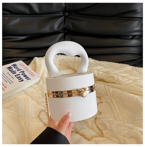 Detail view of the white cylindrical handbag with gold chain on a black leather sofa