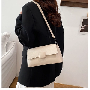 Detail einer cremefarbenen Lackledertasche mit quadratischer Schnalle auf schwarzem Blazer