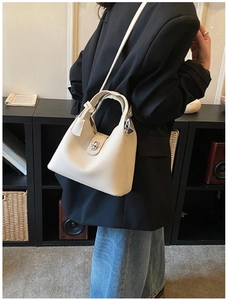 Detail of off-white lychee grain leather bucket bag with silver metal buckle on a model