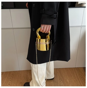 Detail of a cylindrical gold metal handbag with a polished mirror finish and chain