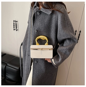 Detail of cream acrylic clutch bag with sculptural gold handle and chain strap on coat