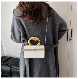 Model wearing a white marble acrylic evening bag with gold handle and chain strap