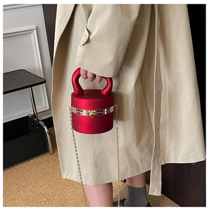 Detail of red cylindrical handbag with gold ring handle and chain strap on khaki coat