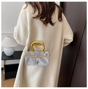 Macro detail of acrylic marble clutch bag with gold U-handle and chain strap