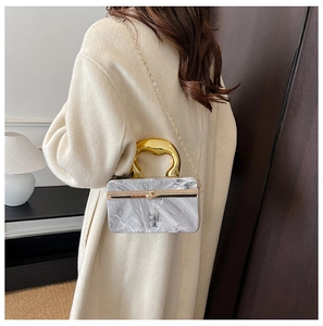 Detail of acrylic evening box bag with marble texture and golden curved handle for women