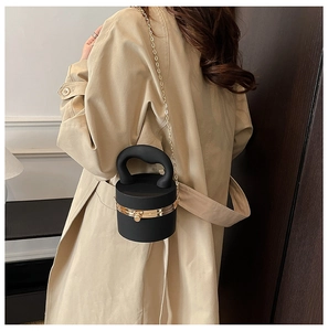 Detail of a black cylindrical crossbody bag featuring a thick curved handle and gold chain