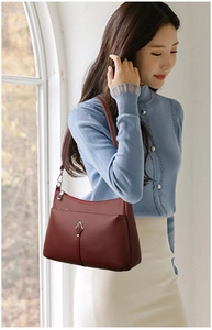 Detail of burgundy lychee leather shoulder bag featuring silver leaf-shaped metal buckle