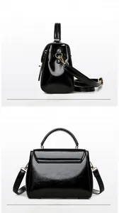 Detail view of glossy black faux leather handbag with golden hardware and long strap