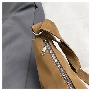 Macro shot of silver metal zipper and wide strap detail on brown crossbody bag