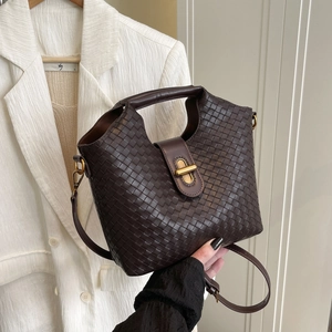 Deep brown woven leather crossbody bag with golden clasp against a white blazer