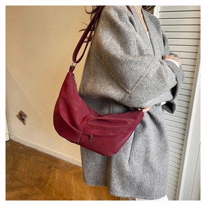 Detail view of burgundy crescent shoulder bag with pleated texture and side zipper