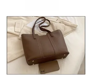 Detail of brown lychee grain tote bag showing white stitching and protective metal feet