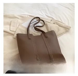 Detail of dark brown pebble leather tote bag with white contrast stitching and metal feet