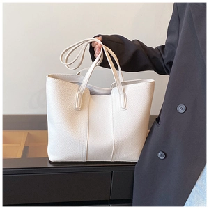 Close-up of white tote bag with lychee texture held by a model in a black suit