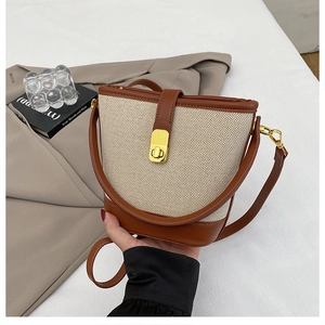 Detail of canvas bucket bag with brown leather trim and golden metal turn-lock closure