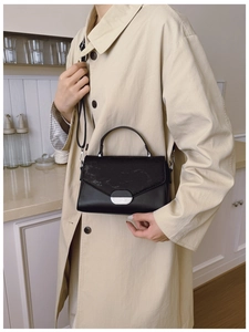 Detail of black crossbody bag with striped textured flap and oval metal buckle on a trench coat