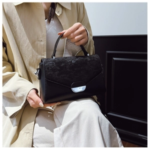 Detail of black crossbody bag featuring textured flap and silver arc metal buckle