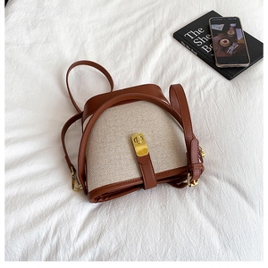 Detail of canvas bucket bag with brown leather trim and golden twist lock closure