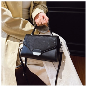 Detail of black crossbody bag featuring textured flap and silver semi-circle metal lock