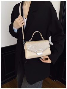 Detail of minimalist beige crossbody bag with silver buckle worn on black blazer