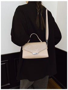 Detail of minimalist cream crossbody bag featuring textured leather and a metal clasp
