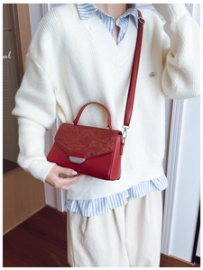 Detail of red textured handbag with silver buckle and adjustable shoulder strap worn by model