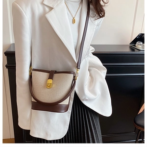 Detail of canvas bucket bag with brown leather trim and golden metal clasp on model