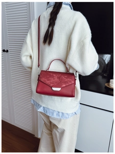 Deep red crossbody bag with silver buckle worn over a white textured sweater