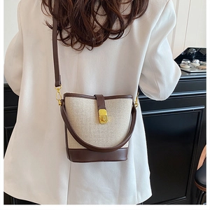Detail of canvas bucket bag with brown leather trim and gold metal lock worn by model