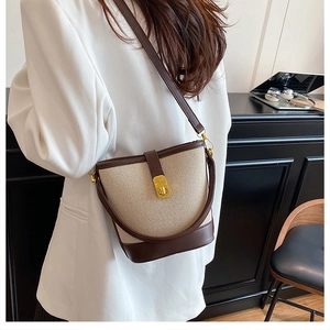 Detail view of canvas and leather bucket bag featuring a gold twist-lock closure and strap