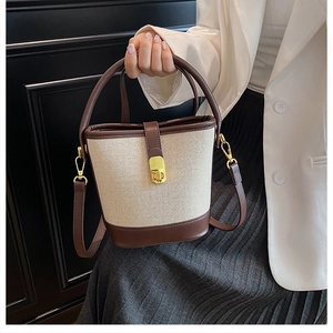 Detail of canvas bucket bag with brown leather trim and golden metal lock clasp