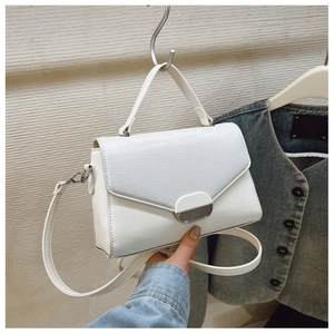 Close-up of white minimalist shoulder bag with textured flap and silver metal buckle