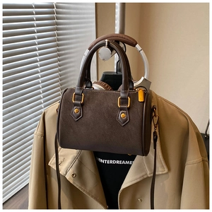 Detailansicht der braunen Zylindertasche mit goldener Hardware und Lederriemen