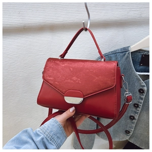 Detail of red crossbody bag featuring textured flap and elegant oval metal buckle