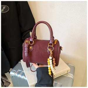 Nahaufnahme einer weinroten Zylindertasche aus Leder mit feiner Textur und Perlenanhänger