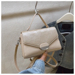 Detail of beige structured handbag featuring striped texture and oval metallic clasp