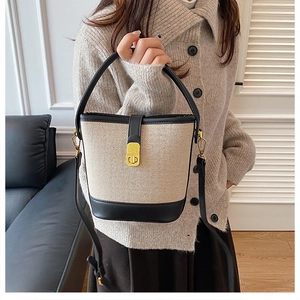 Detail of beige canvas and black leather bucket bag with golden buckle lock and dual straps