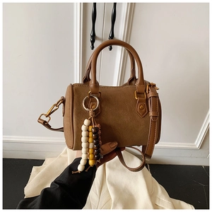 Detailansicht der braunen Zylindertasche mit Holzperlenanhänger und Schultergurt