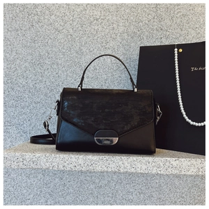 Minimalist black leather handbag with textured flap and silver metal lock on stone step