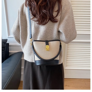 Detail of canvas bucket bag with black leather trim and golden twist lock on a shoulder strap