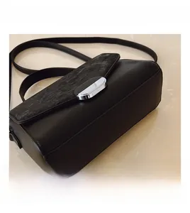 Detail of black leather handbag featuring a textured flap and silver oval metal clasp