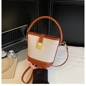 Detail of minimalist bucket bag featuring cream woven texture and brown leather trim