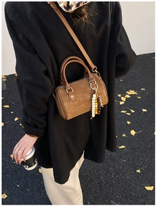 Braune Wildleder-Kissentasche mit Perlenanhänger und Golddetails auf Herbststraße