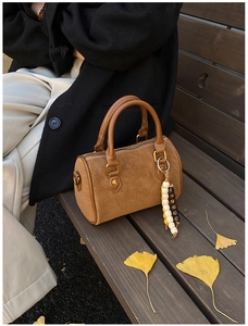 Nahaufnahme der braunen Wildleder-Boston-Tasche mit Perlenanhänger auf Ginkgoblättern