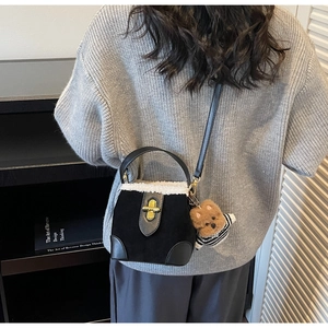 Detail view of black suede crossbody bag with white shearling trim and teddy bear charm
