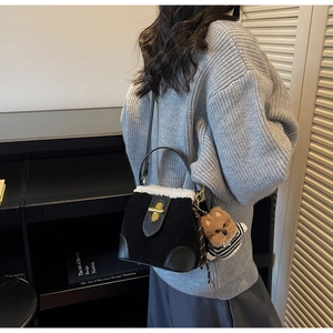 Detailed view of a black suede bag with white faux fur trim and cute bear charm